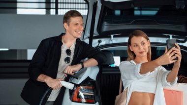 Genç çift EV elektrikli arabasıyla alışveriş merkezinin otoparkına gidiyor şehir merkezindeki şarj oluyor yeşil temiz şarj edilebilir elektrikli araç iç organları ile kentsel sürdürülebilirlik yaşam tarzını gösteriyor