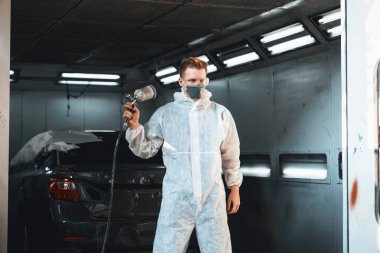 Koruyucu ekipmanlı otomotiv işçisi araba kaportasına sprey tabanca ya da oda atölyesindeki solunum boyasıyla renk boyası uyguluyor. Tamir için araba boyama servisi. Oxus.