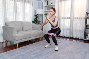 Güçlü enerjik kadın bacak kası kazanmak için direnç bandıyla evde egzersiz yapıyor. Genç atletik Asyalı kadın dayanıklılığı ve dayanıklılık antrenmanı..
