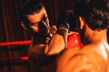 Asyalı ve Kafkasyalı Muay Thai boksörü boks maçında dirsek atağı yapıyor. Güçlü kaslı bir boksör acımasız bir dövüş hüneriyle yumruk ve dirsek yumruğa dövüşüyor. Impetus