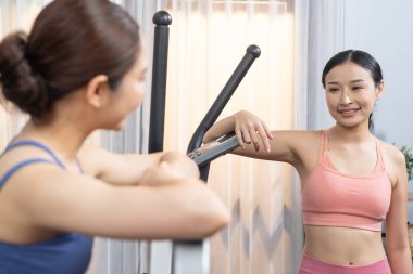 Enerjik ve güçlü atletik Asyalı kadın evde spor arkadaşı ya da antrenörü ile birlikte eliptik koşu makinesiyle koşuyor. Formda fiziğin takibi ve sağlıklı yaşam tarzına bağlılık. Kuvvetli