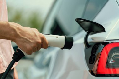 Dışarıdaki şarj istasyonundan EV şarj aletini şarj etmek için elektrikli araca elle tak. Alternatif temiz ve sürdürülebilir enerji kavramına sahip taze gün ışığı ortamı. Kalıcı