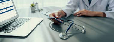 Steteskoplu bir doktor, hastane doktorlarının muayenehanesinde etkili bir sağlık tedavi planı için detaylı tıbbi raporu dizüstü bilgisayarla gözden geçirir ve hastalık teşhisi koyar. Neoterik