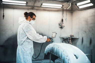 Koruyucu ekipmanlı otomotiv işçisi araba kaportasına sprey tabanca ya da oda atölyesindeki solunum boyasıyla renk boyası uyguluyor. Tamir için araba boyama servisi. Oxus.