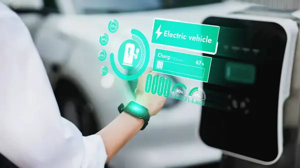 Businessman check EV car battery status on smartwatch hologram while recharge from charging station city car park. Futuristic lifestyle of clean energy for EV tech adaptation. Peruse