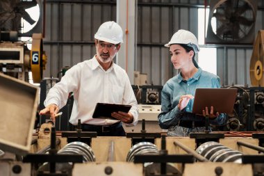 Metal imalatında makine mühendisliği denetleyicisi olarak liderlik örneğini sunan çelik endüstriyel makineyi incelemek için dizüstü bilgisayar kullanan fabrika mühendisi ve asistan..