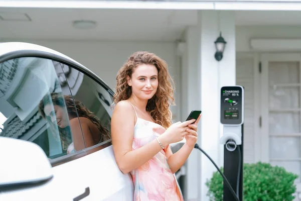 现代环保妇女从家用电动汽车充电站为电动汽车充电 创新的电动汽车技术用于跟踪能源使用情况 以优化国内的电池充电 同步操作 — 图库照片