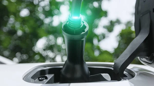 Ev充電器は電気充電ステーションで電気自動車に木のクローズアップの下で光るライト ケーブルによって差し込みます グリーンエネルギーの持続可能性の最先端のイノベーション — ストック写真