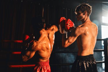 Asyalı ve Kafkasyalı Muay Thai boksörü boks antrenmanında dirsek atağı yapıyor, antrenörlerine dirsek darbesi yapıyor, boks tekniği ve becerilerini sergiliyor. Impetus