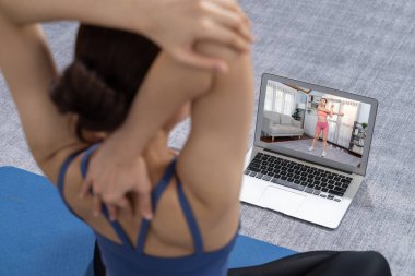 Spor kıyafetli Asyalı bir kadın spor salonunda antrenman yaparken spor minderinde yoga yapıyor. Sağlıklı vücut bakımı kadın dizüstü bilgisayardan yoga videosu izliyor. Kuvvetli