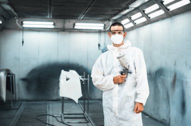 Koruyucu ekipmanlı otomotiv işçisi araba kaportasına sprey tabanca ya da oda atölyesindeki solunum boyasıyla renk boyası uyguluyor. Tamir için araba boyama servisi. Oxus.