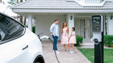 Bulanık arka planda, modern çevre ailesi için alternatif ve sürdürülebilir enerjiyle çalışan EV otomobil için ev şarj istasyonundan odaklanmış elektrikli araç şarj bataryası. Panorama Eşzamanlaması