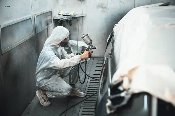 Automotive service worker in full protective gear expertly apply color paint in to cars bodywork with spray gun or respirator painting in chamber workshop. Car paint service for scratch refinish.Oxus