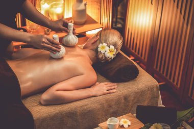 Sıcak bitkisel top spa masaj vücut tedavisi, masör kadın vücuduna nazikçe şifalı bitki torbası bastırıyor. Aromaterapi tesisinin sakinliği ve dinginliği kaplıca salonundaki mumların sıcacık ışığında. Sessiz.