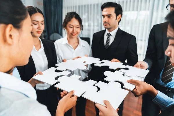 Multiethnic business people holding jigsaw pieces and merge them together as effective solution solving teamwork, shared vision and common goal combining diverse talent. Meticulous