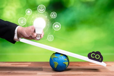 İş adamı ampulü CO2 emisyon ikonu ile ölçekte dengeleyerek, temiz enerji teknolojisi yoluyla karbon azaltımına ilişkin ESG kararlılığı ve çevresel muhafazakar fikir kavramını göstermektedir. Boşluk