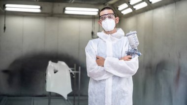 Koruyucu ekipmanlı otomotiv işçisi araba kaportasına sprey tabanca ya da oda atölyesindeki solunum boyasıyla renk boyası uyguluyor. Tamir için araba boyama servisi. Oxus.