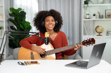 Genç Afrikalı Amerikalı müzisyenin sunucu kanalı gitar çalıyor, şarkı söylüyor, stüdyoda dizüstü bilgisayardan yayın yapıyor. Kulaklık dekorasyonu ve mikrofon kaydı. Tatlandırıcı.