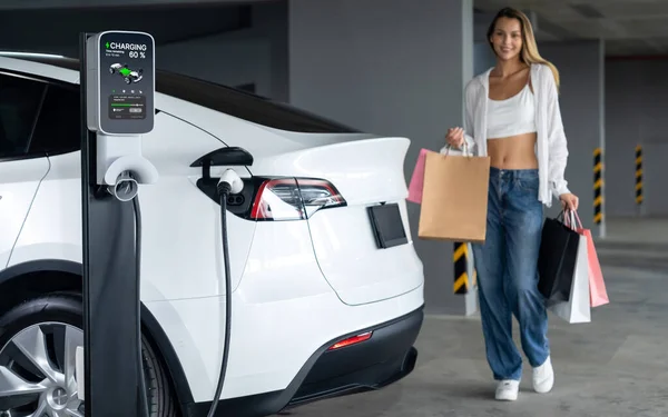 若い女性はEv電気自動車で街の中心部の駐車場に充電し 電気自動車の旅館の緑のきれいな再充電可能エネルギーによって都市の持続可能性のライフスタイルを示しています — ストック写真