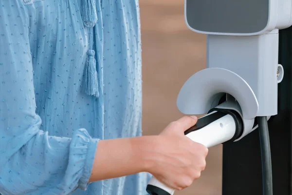 Hand insert EV charger plug into electric vehicle to recharge EV car battery from outdoor charging station. Fresh daylight environment with alternative clean and sustainable energy concept. Perpetual