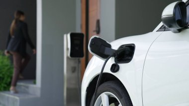 İlerici kadın evdeki elektrikli aracına şarj istasyonu fişi takıyor. EV otomobilleri çevreye yararlı temiz ve yeşil enerji kavramı sağlar.