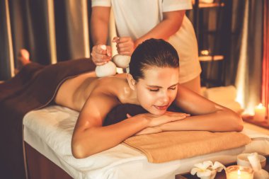 Sıcak bitkisel top spa masaj vücut tedavisi, masör kadın vücuduna nazikçe şifalı bitki torbası bastırıyor. Aromaterapi tesisinin sakinliği ve dinginliği kaplıca salonundaki mumların sıcacık ışığında. Sessiz.