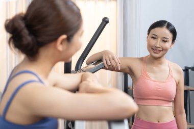 Enerjik ve güçlü atletik Asyalı kadın evde spor arkadaşı ya da antrenörü ile birlikte eliptik koşu makinesiyle koşuyor. Formda fiziğin takibi ve sağlıklı yaşam tarzına bağlılık. Kuvvetli