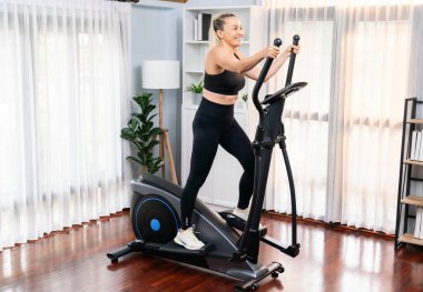 Emeklilerin emekliliğinden sonra sağlıklı bir yaşam tarzı ve vücut bakımı olarak ev portresi çekilen eliptik koşu makinesinde çalışan aktif son sınıf öğrencisi bir kadın. Etki