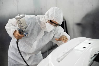 Tam korumalı ekipmanlı otomotiv işçisi sprey tabanca ya da oda atölyesindeki solunum cihazı boyasıyla araba kaportasına ustalıkla renk boyası uygular. Tamir için araba boyama servisi. Oxus.