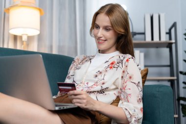 Genç mutlu kadın internetten alışveriş yaparak ürün satın alırken aynı zamanda internet üzerinden online ödeme sistemi ile çevrimiçi mağaza platformundan en yüksek siber güvenlik tarafından korunan ürünler sipariş ediyor.