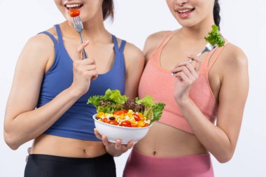 Spor kıyafetli iki genç Asyalı kadın ellerinde meyve ve sebze dolu salata kasesi tutuyorlar. Doğal gençlik ve formda yaşam tarzı izole edilmiş arka planda dengeli beslenen insanlar. Kuvvetli