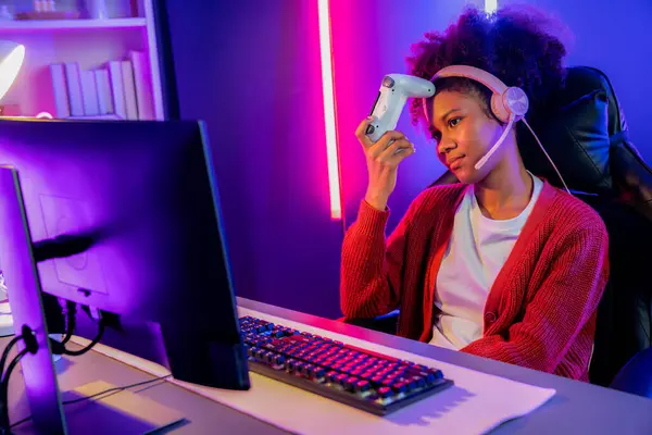 African American girl streamer disappointed playing online fighting with Esport skilled team wearing headphones in neon room. Talking other players planing strategies to win competitors. Tastemaker.
