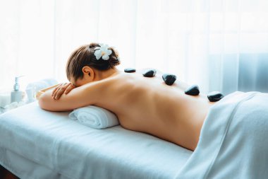 Lüks tatil köyündeki kaplıcalarda sıcak taş masajı. Gün ışığı sükunet ortamında, mutlu kadın müşteri bazalt taş masajından zevk alıyor. Rahatlatıcı bir sıcaklıkla vücudun üzerinde süzülüyor. Sessiz.