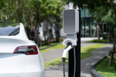 Yazın yeşil sürdürülebilir şehir bahçesinde elektrikli araba şarj oluyor. Kentsel sürdürülebilirlik yaşam tarzı yeşil temiz yeniden şarj edilebilir enerji elektrikli BEV araç iç organları