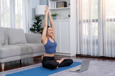 Spor kıyafetli Asyalı bir kadın spor salonunda antrenman yaparken spor minderinde yoga yapıyor. Sağlıklı vücut bakımı kadın dizüstü bilgisayardan yoga videosu izliyor. Kuvvetli