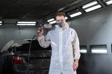 Koruyucu ekipmanlı otomotiv işçisi araba kaportasına sprey tabanca ya da oda atölyesindeki solunum boyasıyla renk boyası uyguluyor. Tamir için araba boyama servisi. Oxus.