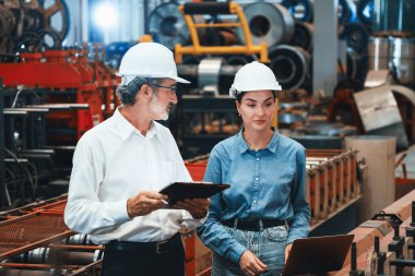 Metal imalatında makine mühendisliği denetleyicisi olarak liderlik örneğini sunan çelik endüstriyel makineyi incelemek için dizüstü bilgisayar kullanan fabrika mühendisi ve asistan..