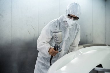 Tam korumalı ekipmanlı otomotiv işçisi sprey tabanca ya da oda atölyesindeki solunum cihazı boyasıyla araba kaportasına ustalıkla renk boyası uygular. Tamir için araba boyama servisi. Oxus.