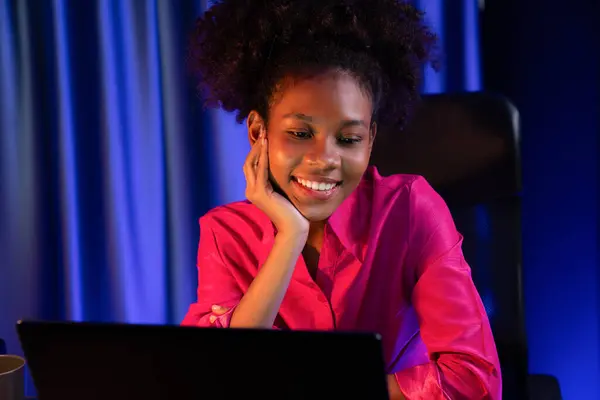 非洲女性博主身穿粉色衬衫 面带笑容 带着有价值的成就项目或获得奖学金 在屏幕笔记本电脑上观看 快乐表达的概念是从家里产生的 节衣店 — 图库照片