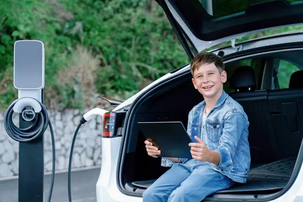 Menino Sentado Porta Malas Carro Usando Tablet Enquanto Recarrega Carro — Fotografia de Stock