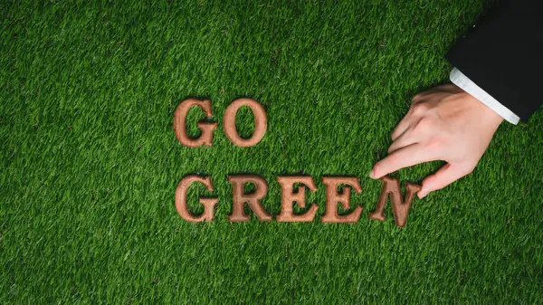 Go green and save the world with environment friendly effort. Message Go Green letter arranged by businessman hand to promote eco awareness for sustainable future with biophilc design background. Gyre