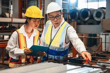 Fabrika mühendisi, metal levha ürünü üzerinde kalite kontrolü yapmak ve ağır endüstriyel çelik damgalama veya oluşturma makinesini denetlemek için iş arkadaşıyla işbirliği yapar. Örnek gösteriliyor