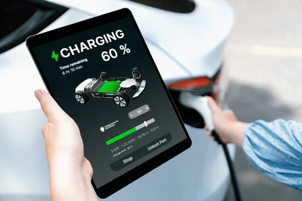 Hand insert EV charger plug into electric vehicle to recharge EV car, battery status display on tablet EV application. Future alternative clean and sustainable energy for transportation. Perpetual