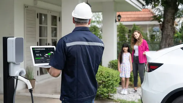 Qualified technician work on home EV charging station installation, make troubleshooting and configuration setup on charging system with laptop for EV at home with family present. Panorama Synchronos