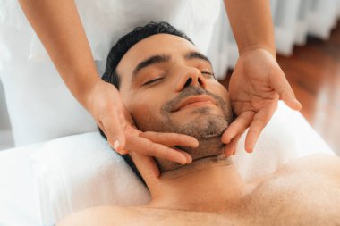 Beyaz adam stres önleyici kafa masajından ve lüks bir tatil beldesi veya otel spa salonundaki modern ışık ortamında yüz güzelliği eğlencelerini şımartmaktan hoşlanıyor. Sessiz.