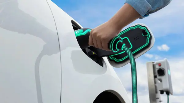 Asian man insert EV charger and recharge his electric car recharging energy from home charging station on sky and cloudscape background. Smart and futuristic home energy infrastructure. Peruse