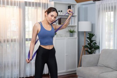 Enerjik kadın evde egzersiz yapıyor, kas kazanmak için direnç bandını esnetiyor. Genç atletik Asyalı kadın dayanıklılığı ve dayanıklılık antrenmanı ev ödevi rutin konsepti olarak..