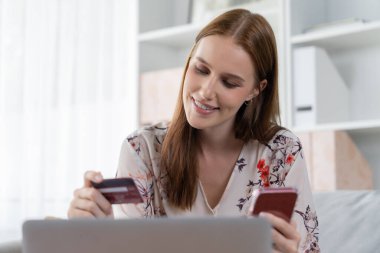 Genç mutlu kadın internetten alışveriş yaparak ürün satın alırken aynı zamanda internet üzerinden online ödeme sistemi ile çevrimiçi mağaza platformundan en yüksek siber güvenlik tarafından korunan ürünler sipariş ediyor.