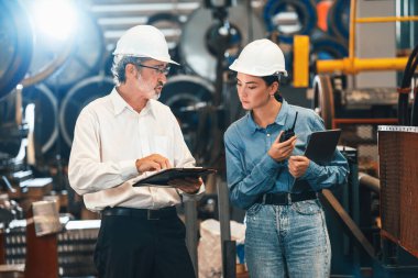 Metal imalatında makine mühendisliği denetleyicisi olarak liderlik örneğini sunan çelik endüstriyel makineyi incelemek için dizüstü bilgisayar kullanan fabrika mühendisi ve asistan..