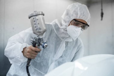 Tam korumalı ekipmanlı otomotiv işçisi sprey tabanca ya da oda atölyesindeki solunum cihazı boyasıyla araba kaportasına ustalıkla renk boyası uygular. Tamir için araba boyama servisi. Oxus.
